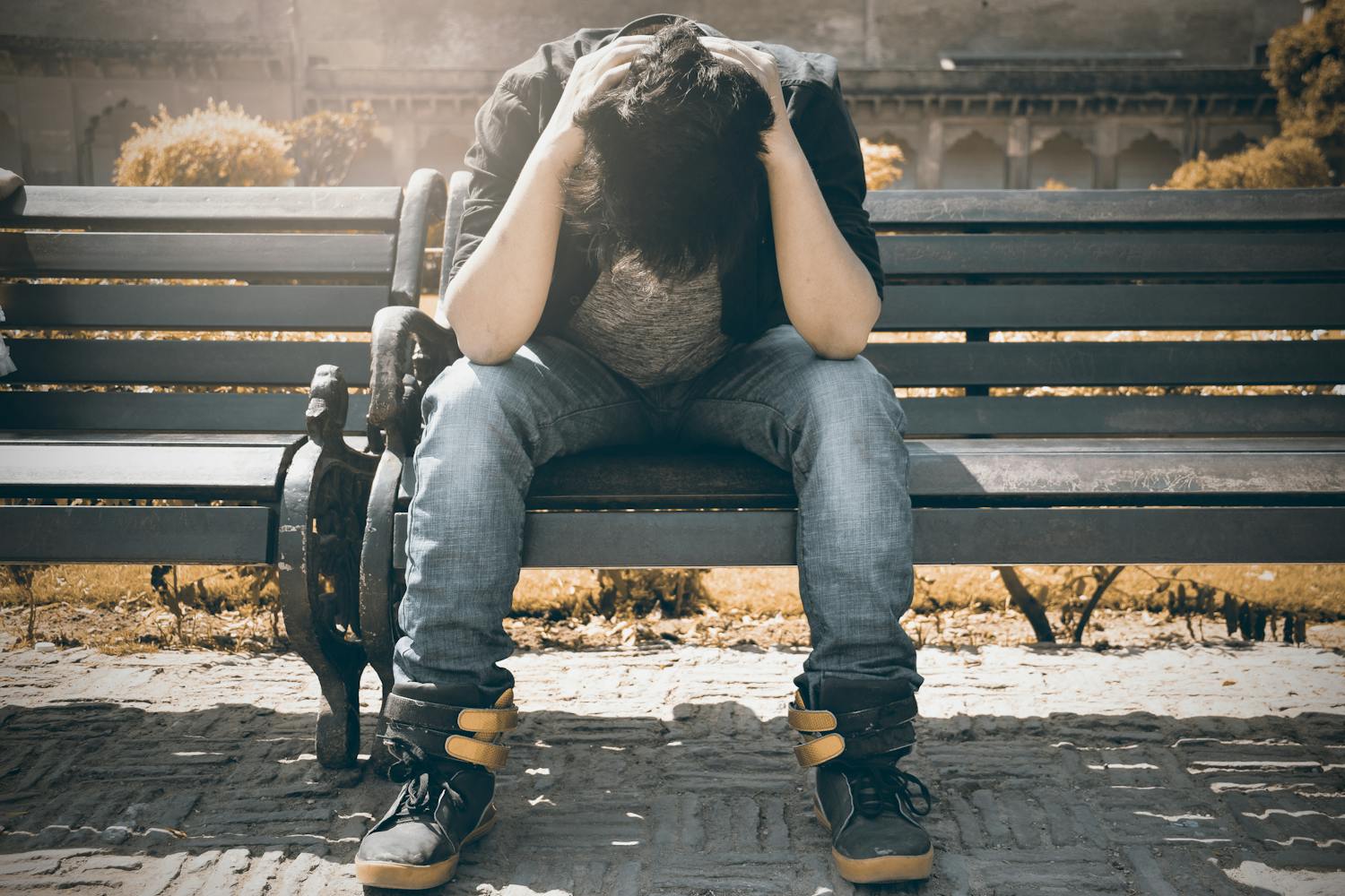 A man on the bench, holding his head because there are many medications that can cause depression.