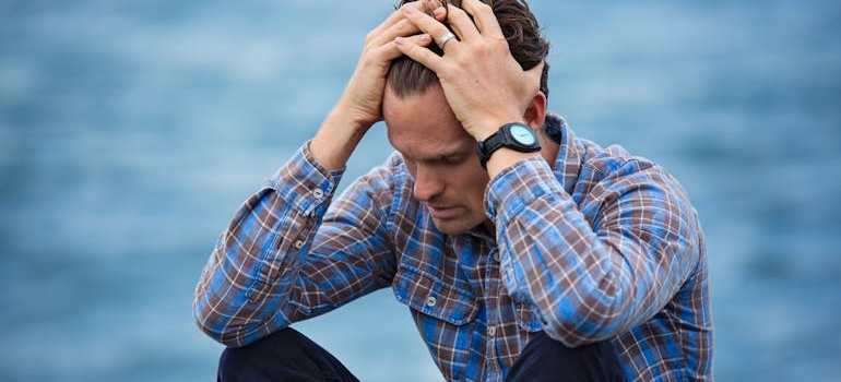 Man sitting by the water and holding his head.