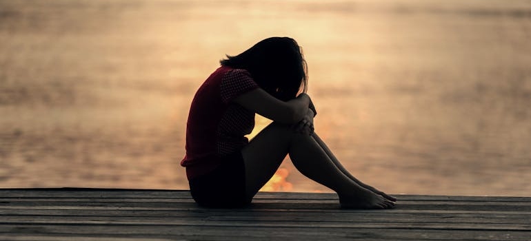 Woman sitting by the water and holding her knees.