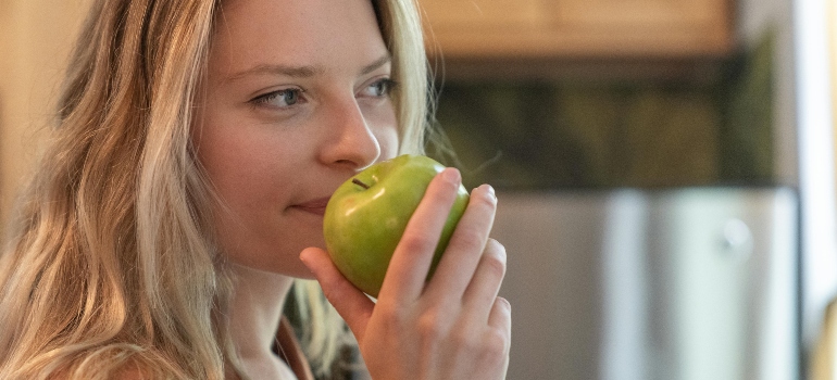 A woman is smelling a green apple.