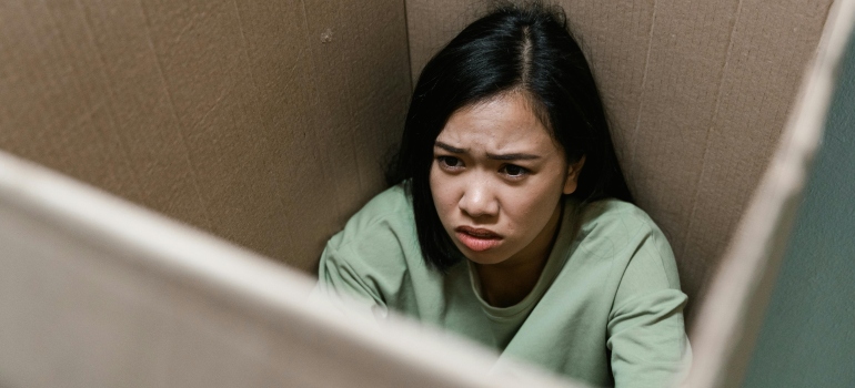 Woman in a green blouse sitting in a carton box thinking about marijuana and panic attacks.