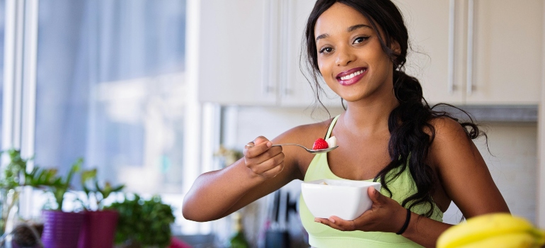 A woman in a green top is holding a white bowl with healthy food and thinking about why nutrition and addiction recovery are connected.