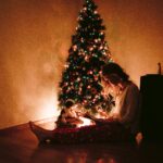 Woman sitting next to a Charistmas tree.