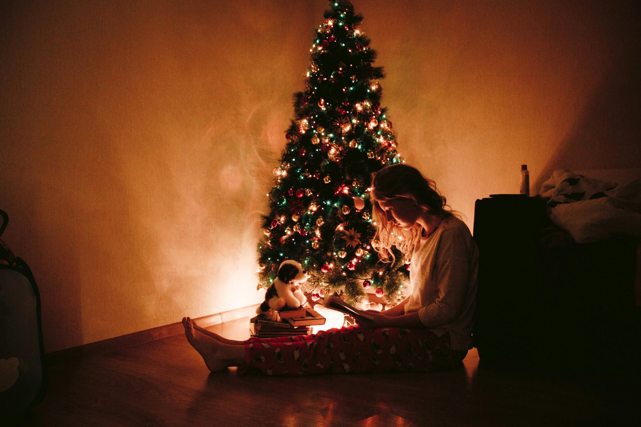 Woman sitting next to a Charistmas tree.