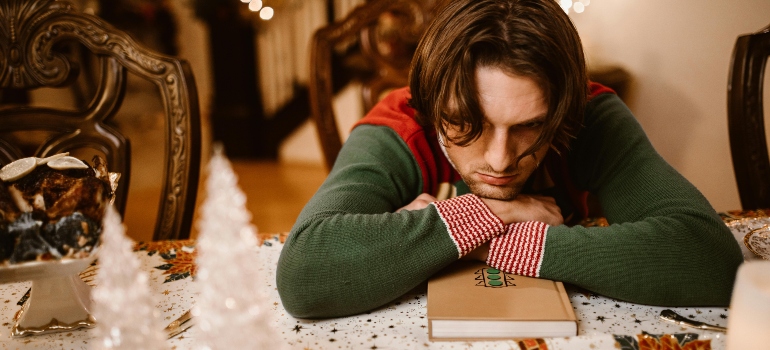 Man leaning his head on a table and experiencing holiday blues symptoms.