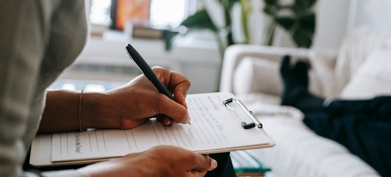 Psychiatrist writing on a clipboard and talking to her client about marijuana and panic attacks.