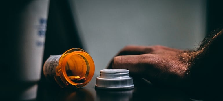 Man's hand next to an open pill bottle.