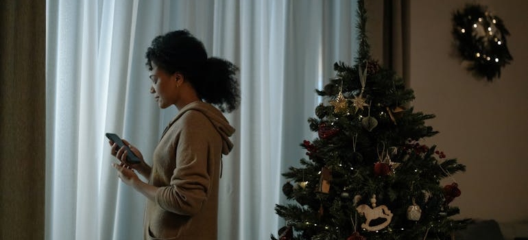 Woman standing next to a Christmas tree and looking out of the window.