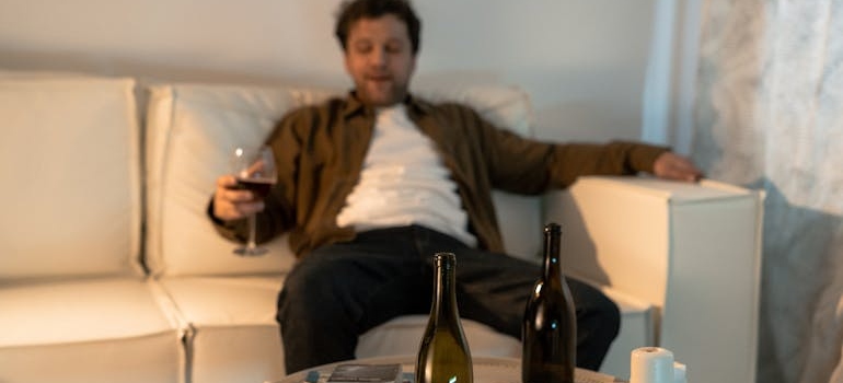 Man sitting on the couch, drinking a glass of wine and struggling with veteran PTSD and substance abuse.