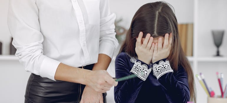 Teacher scolding a young girl who is covering her face.