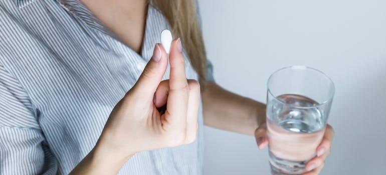 Woman holding a white pill and a glass of water.