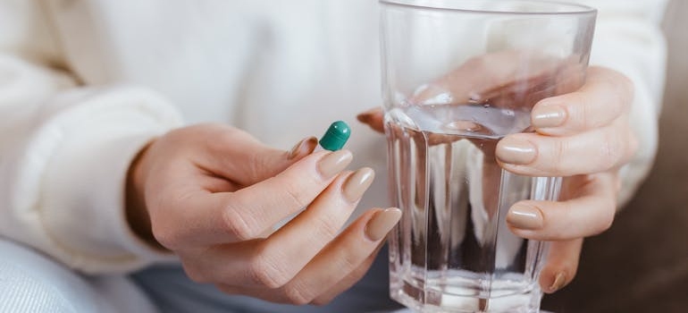 Woman holding a pill and a glass of water.