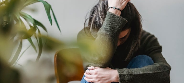 Woman sitting on a chair and holding her head while experiencing anxiety, one of Demerol withdrawal symptoms.