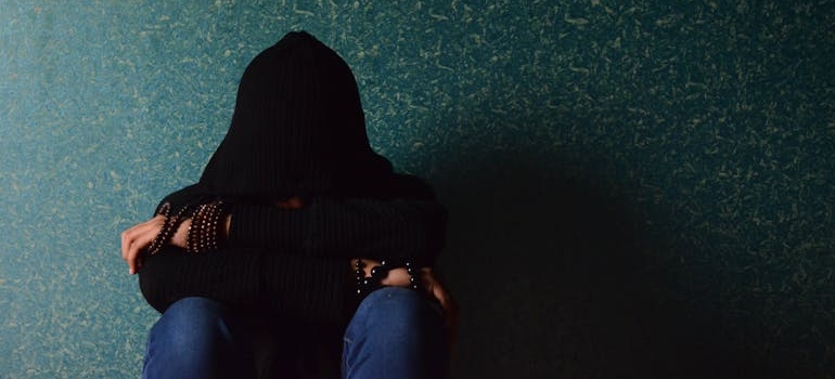 Person sitting next to a wall, struggling with depression due to inhalant abuse.