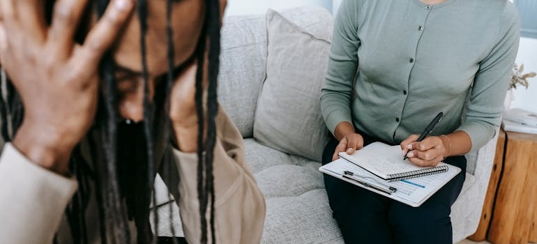 Therapist writing in a clipboard while talking to a distressed patient.