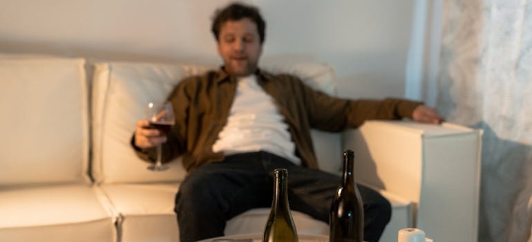 Man sitting on the couch, drinking wine and struggling with mental health issues and addiction.