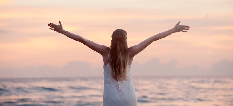 Woman with raised arms looking at the sea.