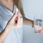 Woman holding a glass of water and a white pill.