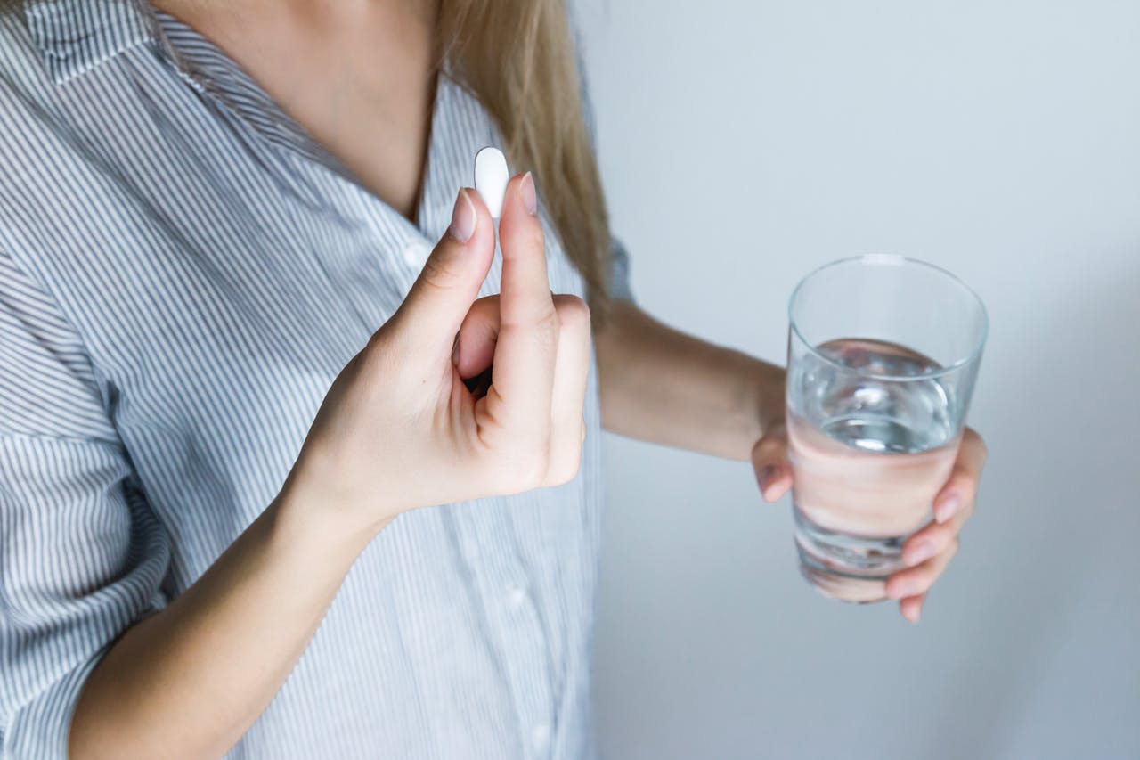 Woman holding a glass of water and a white pill.