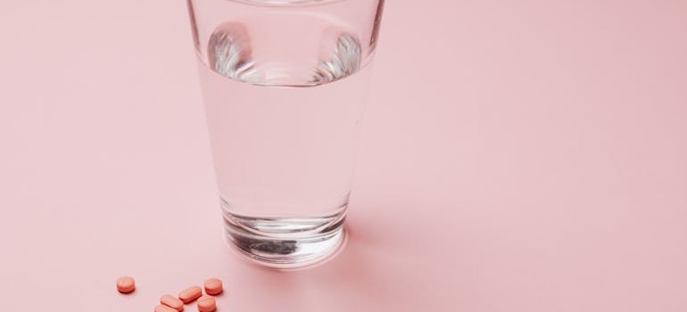 Glass of water next to pink pills.