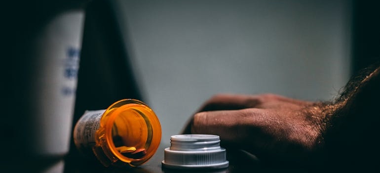 Person's hand next to a spilled pill bottle.