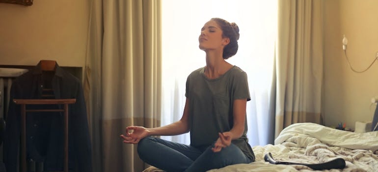 Woman sitting on the bed and meditating to achieve long term sobriety.