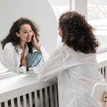 Woman looking in the mirror smiling and practicing self-forgiveness in recovery.