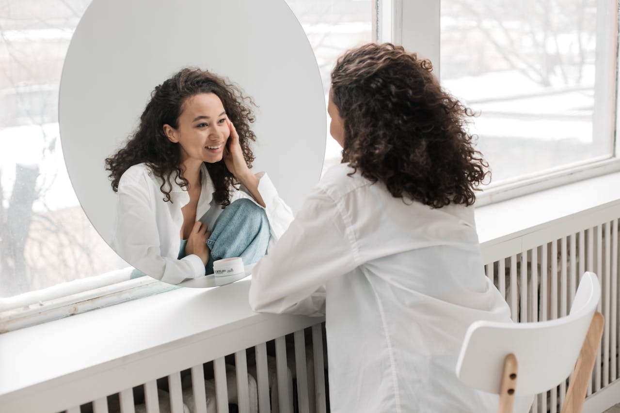 Woman looking in the mirror smiling and practicing self-forgiveness in recovery.