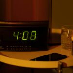 Alarm clock, pills and a phone on a nightstand,