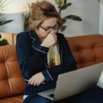 Woman hugging an alcohol bottle while looking at her laptop.