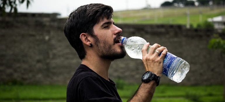 Man drinking a bottle of water after learning how to get weed out of your system.