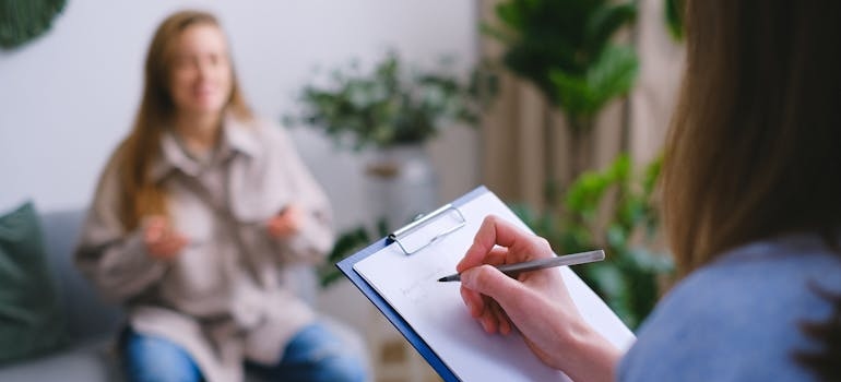 Woman writing in a clipboard answers to FAQs about addiction treatment.