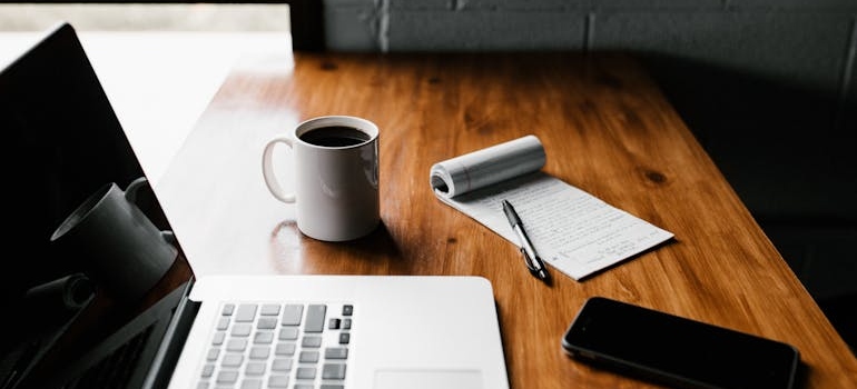 Laptop next to a notepad and a pen.
