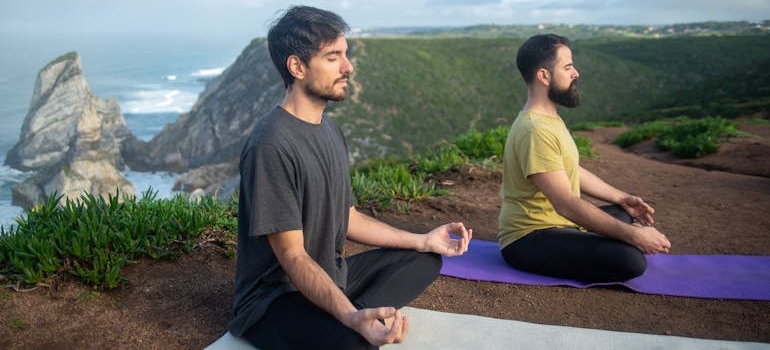 Men sitting on the cliff and doing yoga.