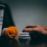 Hand next to a spilled pill bottle.