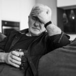 Man sitting on the couch drinking a glass of wine while struggling with PTSD and alcohol issues.