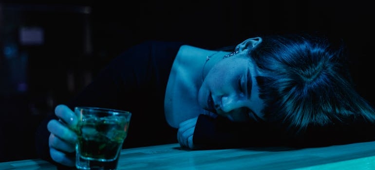 Woman drinking a glass of whiskey and lying on the bar.
