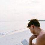 Man reading best stress management books on a beach.