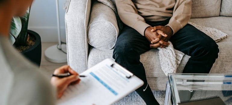 Therapist writing in a clipboard while talking about benefits of sobriety with a patient.