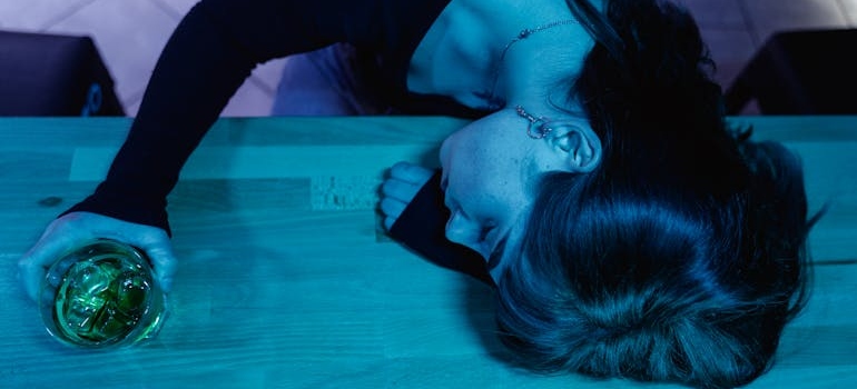 Woman sitting at a bar and drinking a glass of whiskey while experiencing alcohol poisoning.