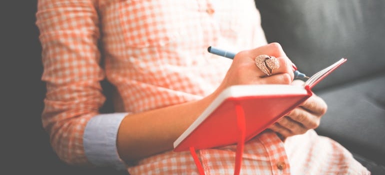 Woman journaling in a red notebook.