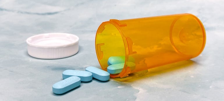 Blues drugs spilling out of an orange prescription bottle.
