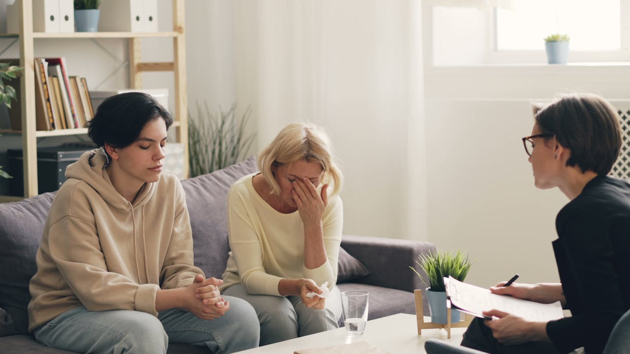 Parents of addicts crying in a therapy session with their addicted child.