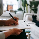 Woman writing in a clipboard while talking to a client and doing an evaluation.