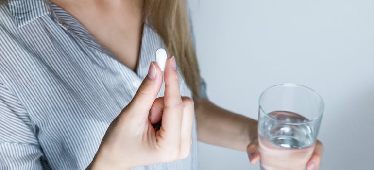 Woman holding a pill and a glass of water.