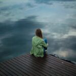 Woman sitting at a dock and looking out at the lake while struggling with seasonal affective disorder and addiction.