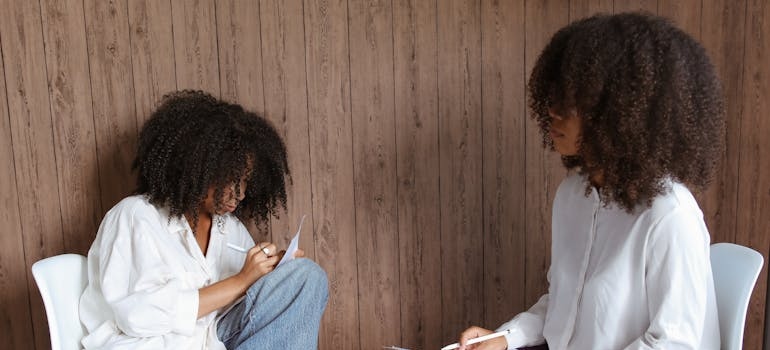 Woman writing on a piece of paper while talking to a therapist.