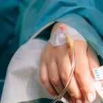 Patient lying in a hospital bed with an IV in their hand.