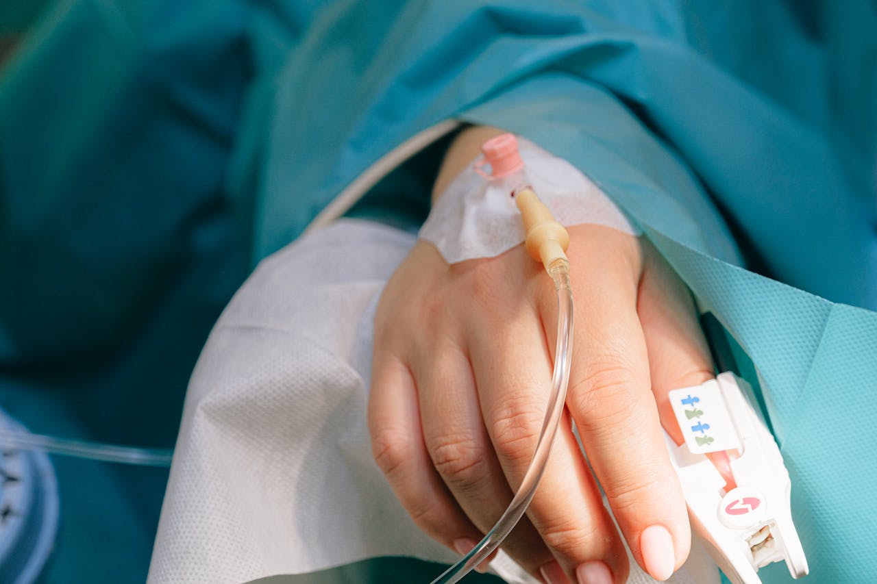 Patient lying in a hospital bed with an IV in their hand.