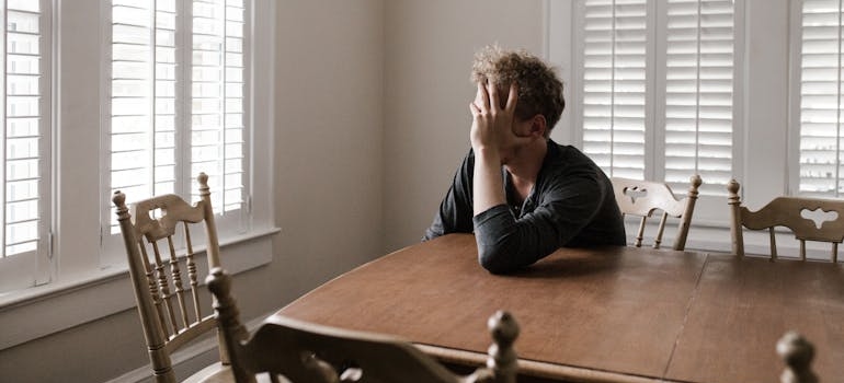 Man sitting at the kitchen table holding his face with his hand.